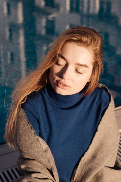 beautiful young blond model girl enjoys the warmth and sunshine by the blue pool, closed her eyes - Foto, afbeelding