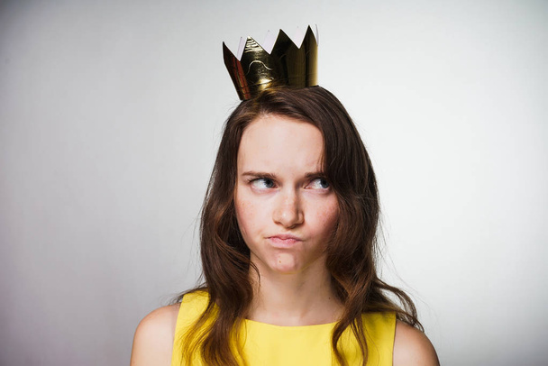 disgruntled pensive young woman in a yellow dress thinks about something, on her head a golden crown - Foto, afbeelding
