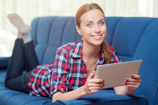 Happy young woman with tablet pc laying on sofa a home - Foto, imagen