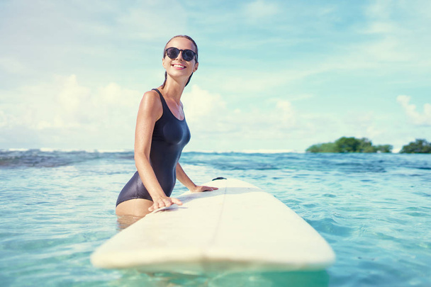 saludable atlético joven surfista chica con sexy ajuste cuerpo celebración surf tablero mientras de pie en agua clara
 - Foto, imagen