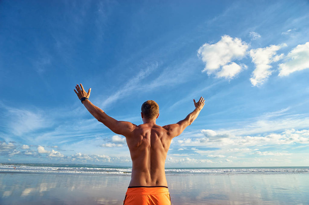 Young handsome strong man raising hands up on the beach against sky. - Foto, Bild