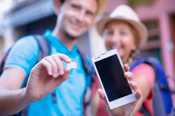 Young couple of travelers showing sim-card and screen of smartphone - Foto, imagen