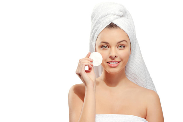 Smiling young woman with a towel on her head, healthy pure skin and removes makeup from the face with cotton pad on white background - Φωτογραφία, εικόνα