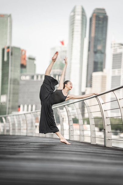 Hermosa joven bailando en la ciudad, vestida de negro, con fondo de rascacielos
  - Foto, imagen
