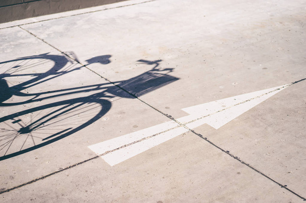 Shadow of bicycle on the ground and white arrow - Zdjęcie, obraz