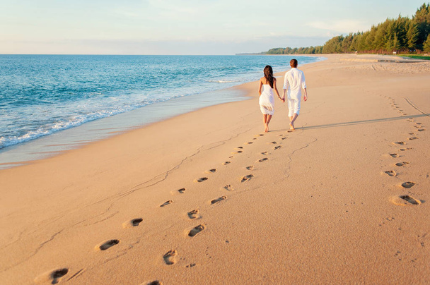 Back view of loving couple walking away with footprints at sandy beach - Fotoğraf, Görsel