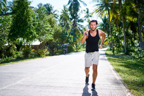 Young strong man is running under palm trees. - Фото, изображение