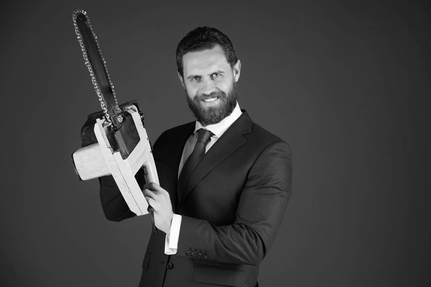 chainsaw for everyone. happy man or bearded businessman hold yellow chainsaw in outfit - Фото, изображение