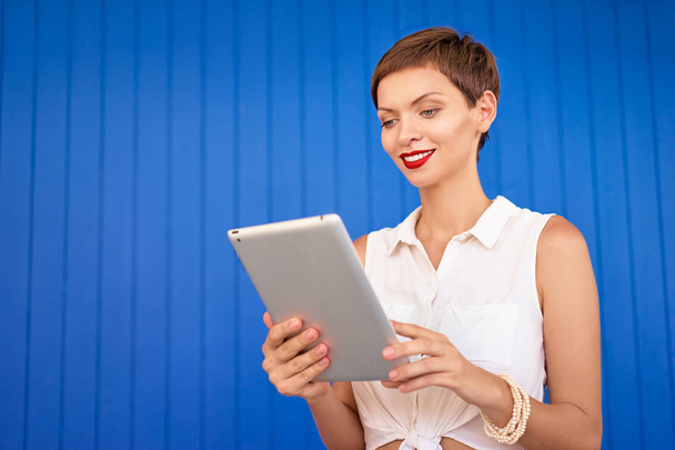 Colorful portrait of pretty young woman using tablet computer against blue wall. - Foto, Imagem
