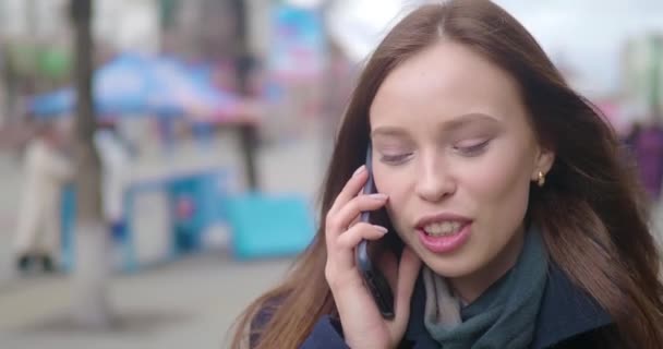 Attractive and cheerful young woman using a cell phone outside. She is talking on the phone and laughing. Crowded city street. Close up. - Materiał filmowy, wideo