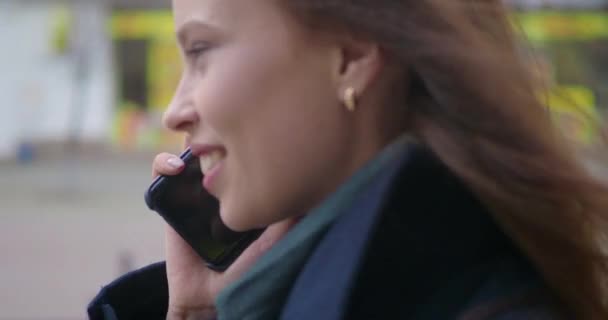 Viehättävä ja iloinen nuori nainen käyttää matkapuhelinta ulkona. Hän puhuu puhelimessa ja nauraa. Täpötäysi katu. Sulje se.
. - Materiaali, video