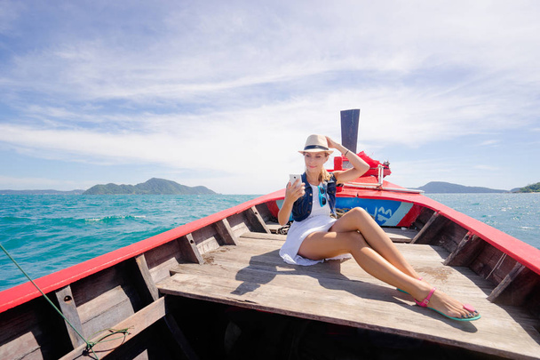 Denizin üzerinde geleneksel longtail tekne yelken smartphone kullanan genç ve güzel kadın. - Fotoğraf, Görsel