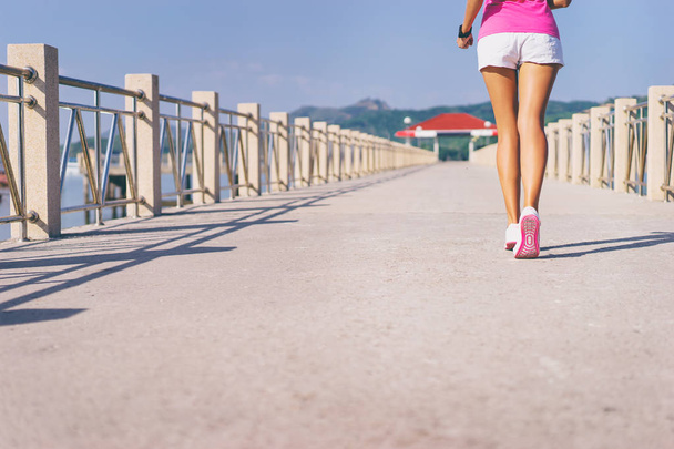 Young slim woman exercising on the sea pier. Female feet in sneakers outdoor. - Foto, afbeelding