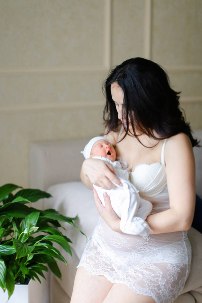 Молодая европейская мать в белой одежде держит новорожденного ребенка
. - Фото, изображение