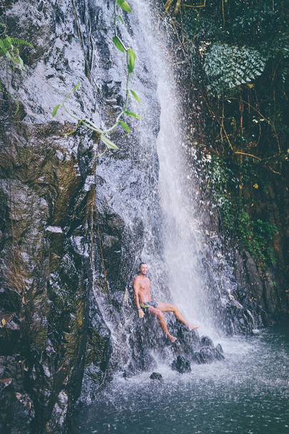 Szczęśliwy młody człowiek relaksujący pod tropikalnym wodospadem  - Zdjęcie, obraz
