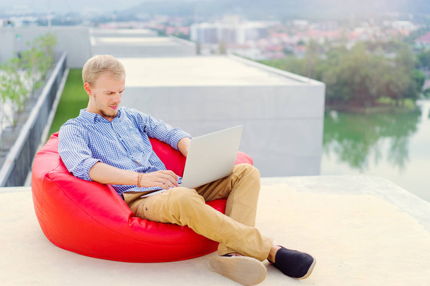 Jonge knappe man aan het werk op laptop zittend op het dak. - Foto, afbeelding