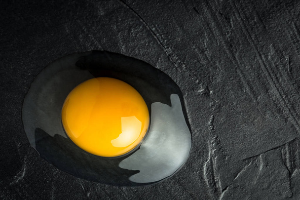 Broken Raw Egg Yolk on Dark Stone Background - Fotografie, Obrázek
