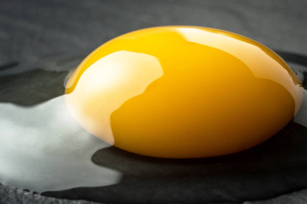 Yema de huevo roto crudo sobre fondo de piedra oscura. Alimentos orgánicos frescos
 - Foto, Imagen