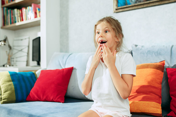 Little surprised teen girl watching tv at home. - Фото, изображение