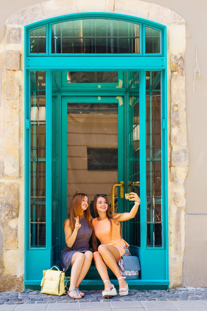 hermosas chicas sentadas en las escaleras cerca de las puertas de vidrio y hacer selfie
 - Foto, Imagen