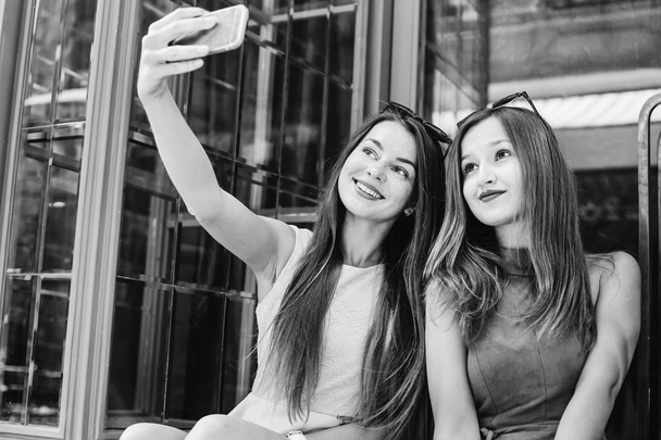 Niedliche Mädchen mit Sonnenbrille auf dem Kopf machen ein Selfie auf dem Hintergrund von Glastüren auf einem Schwarz-Weiß-Foto - Foto, Bild