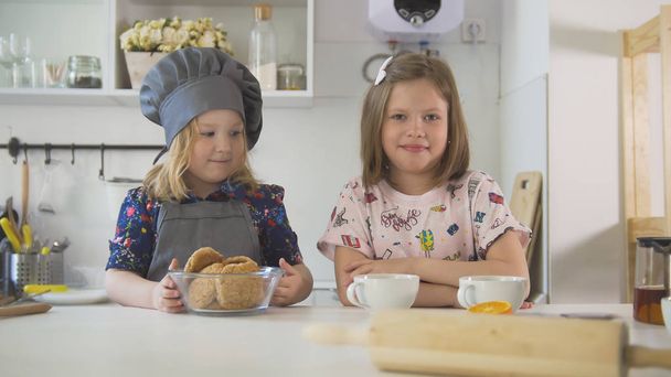 Twee zusjes glimlachend met zelfgemaakte koekjes en kopjes thee bij het koken van de studio - Foto, afbeelding