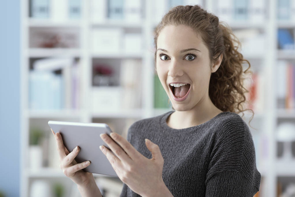 Surprised cheerful girl connecting online with her tablet and playing funny videos, she is enjoying and gasping - Fotoğraf, Görsel