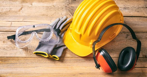Baustellensicherheit. Schutzhelm, Kopfhörer, Handschuhe und Brille auf Holzgrund - Foto, Bild