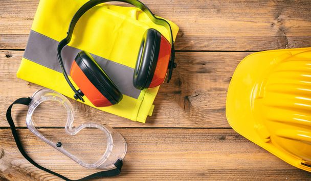 Construction site safety. Protective hard hat, headphones and glasses on wooden background, copy space, top view - Photo, Image
