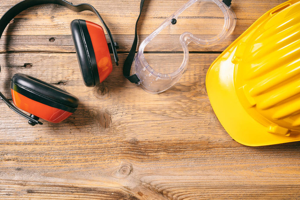 Baustellensicherheit. Schutzhelm, Kopfhörer und Brille auf Holzgrund, Kopierraum, Draufsicht - Foto, Bild