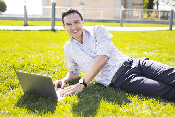 Smiling corporate man wearing hand watch lying on the grass - 写真・画像