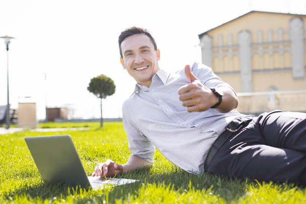 Experienced remote worker using his laptop lying on the grass - 写真・画像