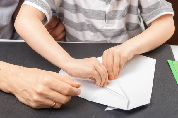 Prozess des Faltens einer Origami-Figur aus weißem Papier zusammen mit einem Kind und einem Erwachsenen. Nahaufnahme. das Konzept der gemeinsamen familiären Kreativität, die Weitergabe von Erfahrungen von Generation zu Generation - Foto, Bild