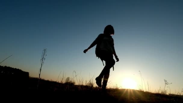 Silueta de mujer alegre con mochila que camina a través del campo de hierba
 - Metraje, vídeo
