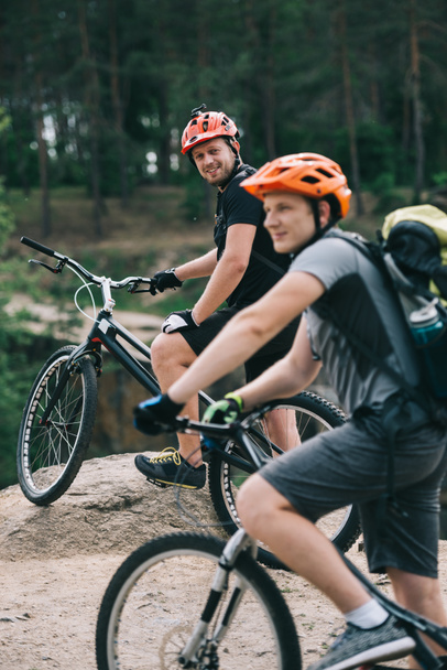 Gelukkig jonge trial bikers permanent op rotsachtige klip met wazig dennenbos op de achtergrond - Foto, afbeelding
