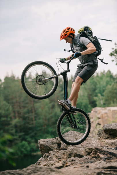 extreme proef biker staande op het achterwiel op rotsachtige klif - Foto, afbeelding