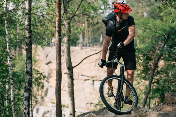 young male extreme cyclist in protective helmet riding on mountain bicycle in forest - 写真・画像