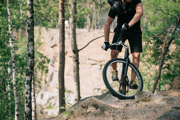 cropped image of male extreme cyclist with backpack doing stunt on bmx in forest - Photo, Image