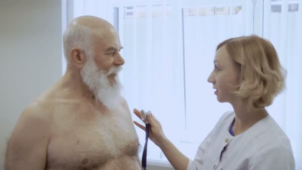 Doctor finished listen senior man with stethoscope. Old man at the reception in cardiologist. Elderly man has a problem with lungs. Doctor tells her conclusion to senior man after chekicing his lungs. - Záběry, video