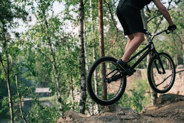 cropped image of male extreme cyclist jumping on mountain bike in forest - Foto, imagen