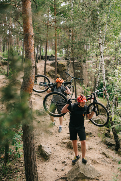 jóvenes ciclistas de trial que llevan bicicletas en las espaldas del bosque
 - Foto, imagen