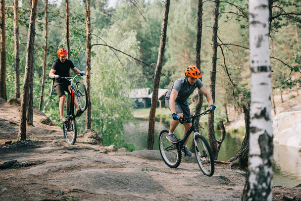 bukósisakot, kiegyensúlyozó, a hátsó kerék, míg barátja, lovaglás a közeli erdőben hegyi kerékpár-férfi extreme kerékpáros - Fotó, kép
