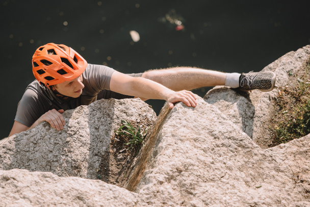 vista ad alto angolo di escursionista maschio concentrato in casco protettivo arrampicata su rocce
  - Foto, immagini