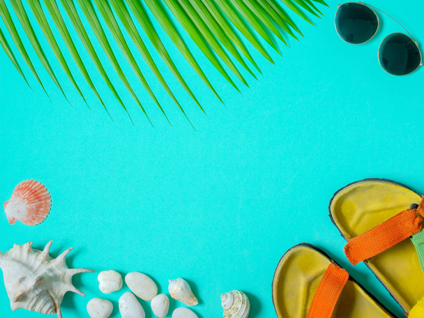 Plochá laických turistické příslušenství, barevné sandál, sluneční brýle s mušle Beach, pláž oblázky a kokosový Palmový list na Aqua modré pozadí s prázdnou textu prostoru. Koncept letní dovolenou pohled shora. - Fotografie, Obrázek