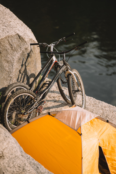 scenic view of two mountain bicycles and tourist tent on rocky cliff over river  - Φωτογραφία, εικόνα