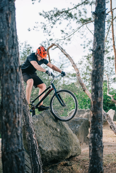 äärimmäinen nuori kokeiluversio moottoripyöräilijä kiipeily kalliolle mäntymetsässä
 - Valokuva, kuva