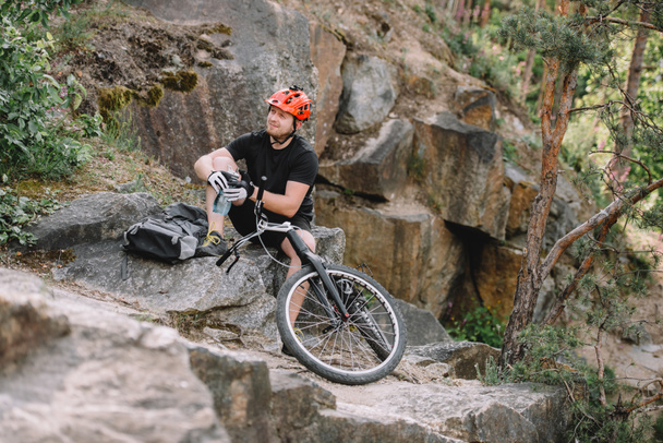 joven ciclista de trial relajándose en las rocas con bicicleta al aire libre
 - Foto, Imagen