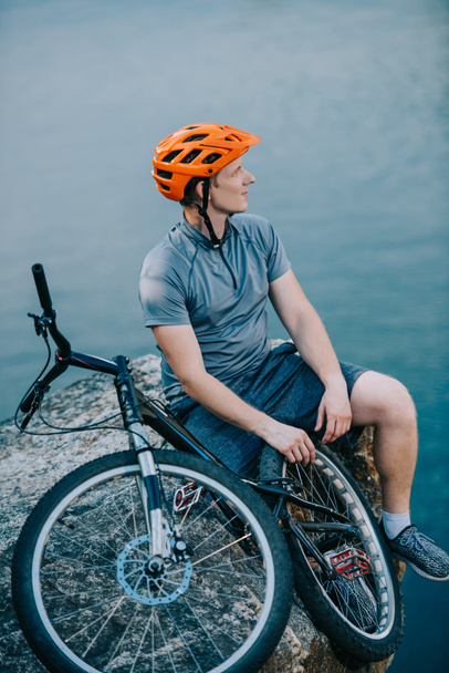 pensativo joven ciclista de prueba relajarse en el acantilado rocoso sobre el agua
 - Foto, imagen
