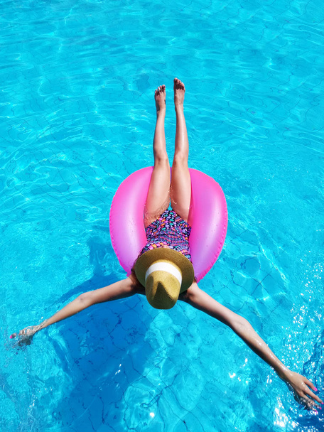 Young beautiful girl relaxing and swimming in the blue swimming pool with a pink circle closeup - Foto, Imagem