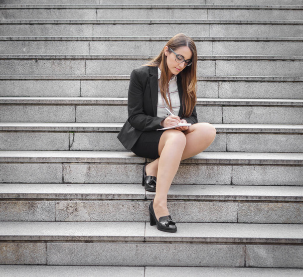 Femme en costume prenant des notes dans les escaliers, jambes croisées
 - Photo, image